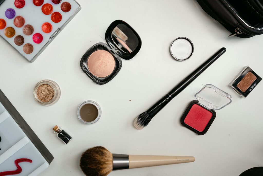 A flat lay of beauty products including eyeshadow, brushes, and blush on a white surface.