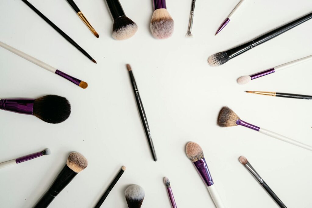 Flat lay of various makeup brushes arranged in a circle on white background.
