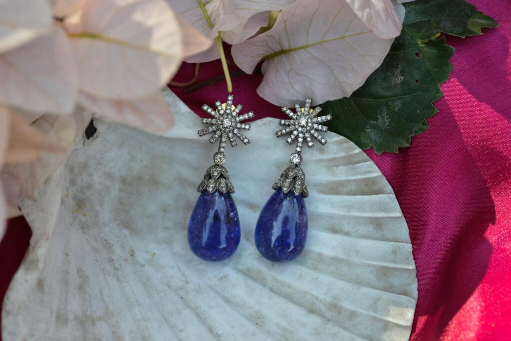 Stunning blue and silver earrings displayed on a seashell with floral background.