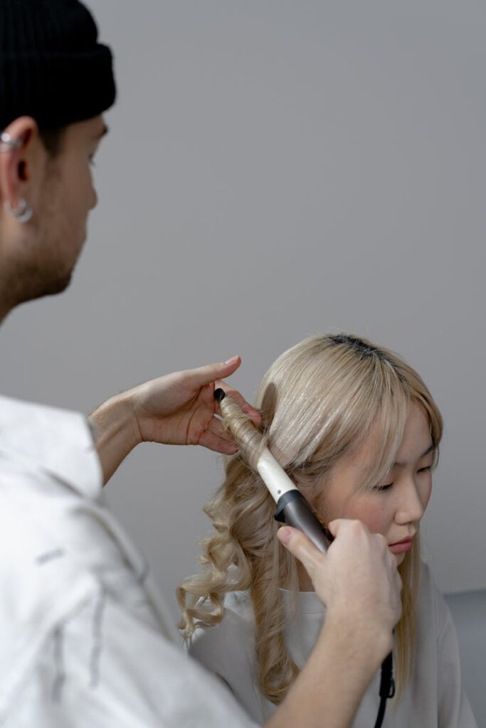Hairstylist curling a client's hair indoors, showcasing modern hairstyling techniques.