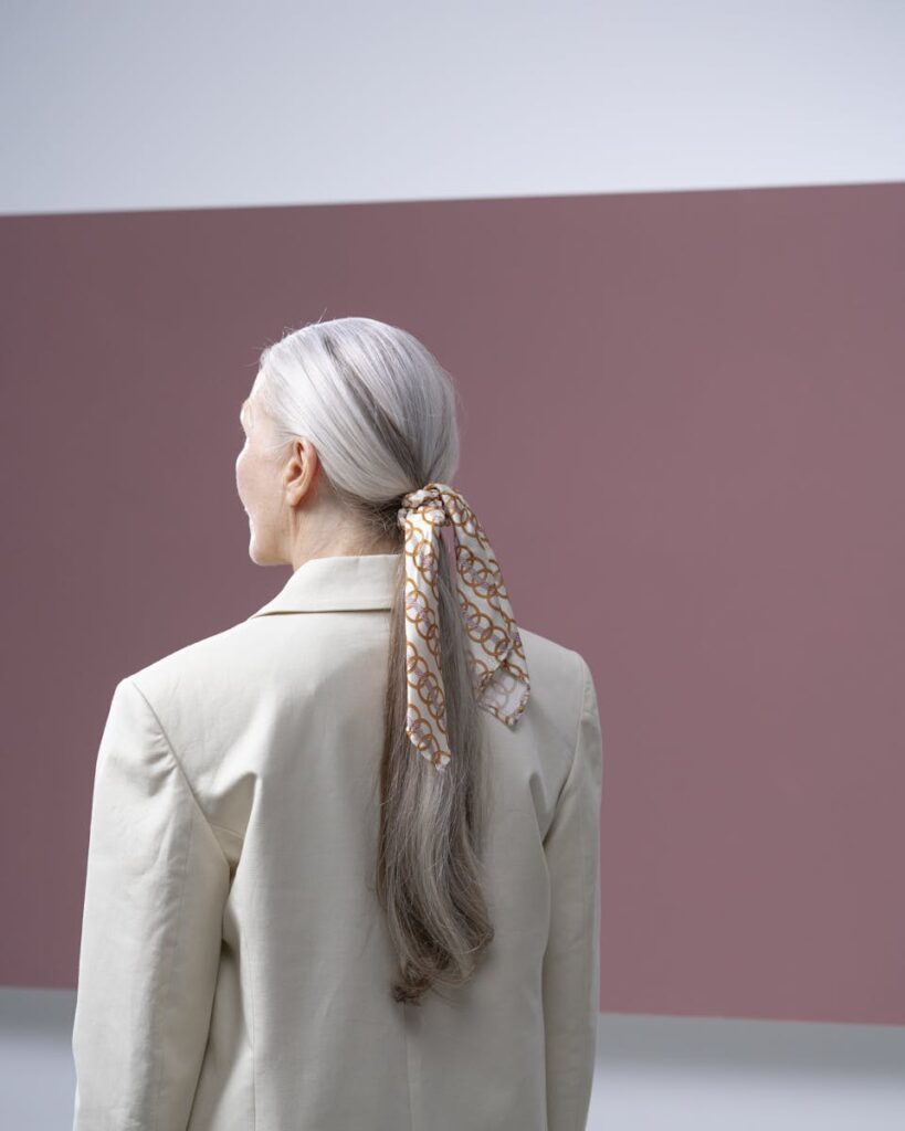 Sophisticated senior woman dressed in a beige blazer with a stylish ponytail and scarf.