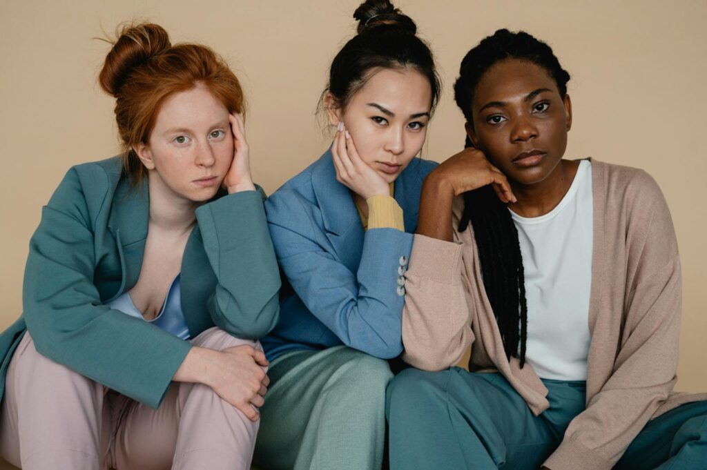 Three diverse women posing confidently in a studio with pastel attire, reflecting diversity and empowerment.
