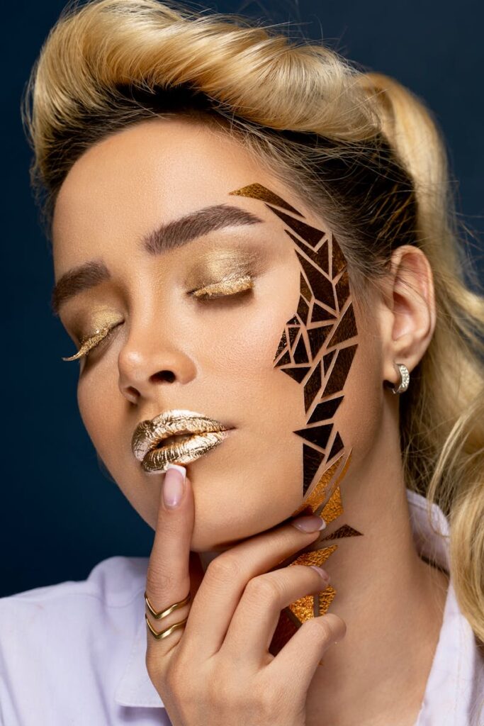 A stunning studio portrait featuring a woman with intricate geometric face art and shimmering golden makeup.