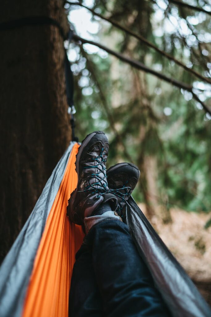 Man relaxing in a hammock with boots in a serene forest setting, ideal for adventure and travel themes.