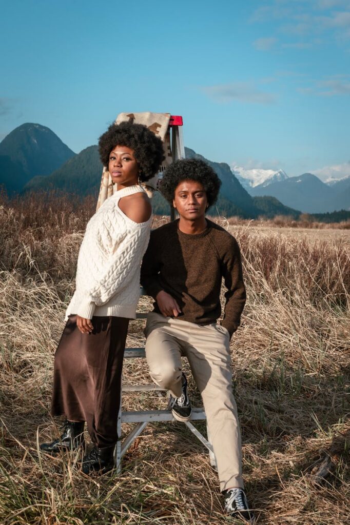 Stylish couple posing outdoors against a mountain landscape with a ladder backdrop.