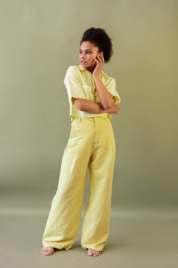 A fashionable Black woman poses confidently in a studio wearing a yellow outfit.
