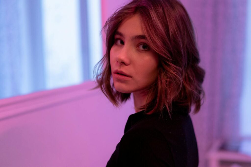 A woman with a bob haircut, gazing softly in ambient pink lighting indoors.