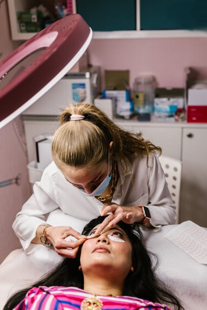 A woman receives an eyelash extension treatment from a beautician at a salon.