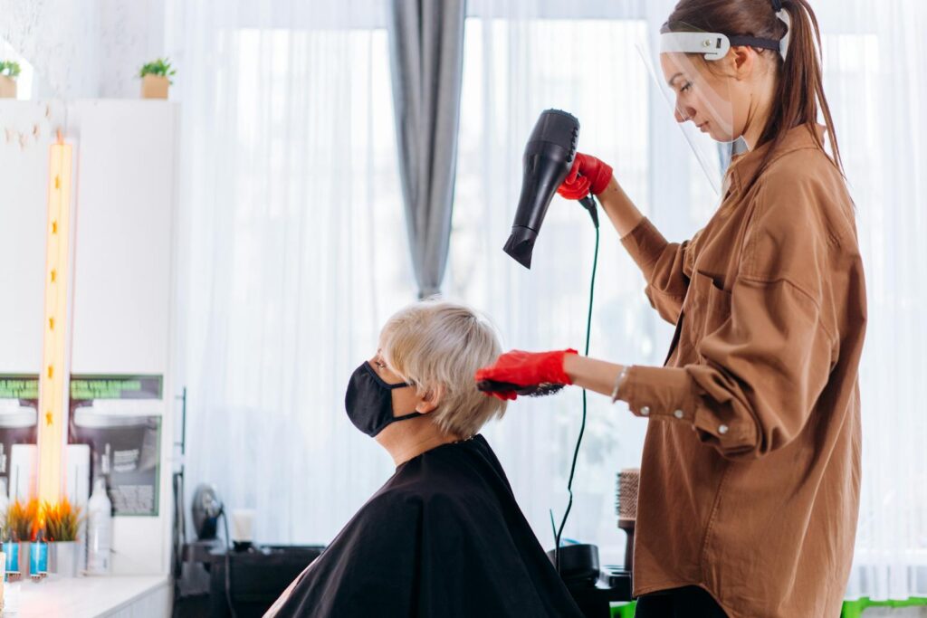 Senior woman gets a stylish haircut indoors by a professional hairstylist wearing protective gear.