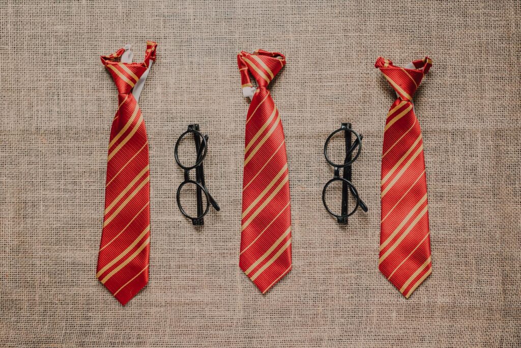 Three striped red ties and black eyeglasses on a textured burlap surface, evoking a wizard theme.