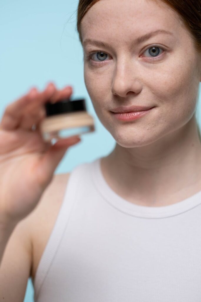 Woman holding a cosmetic product, showcasing natural beauty in a studio setting.
