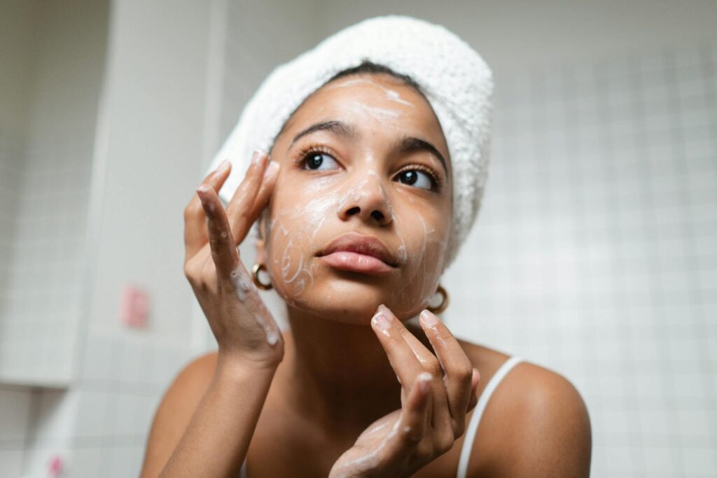 A young woman applies skincare cream in a modern bathroom setting.