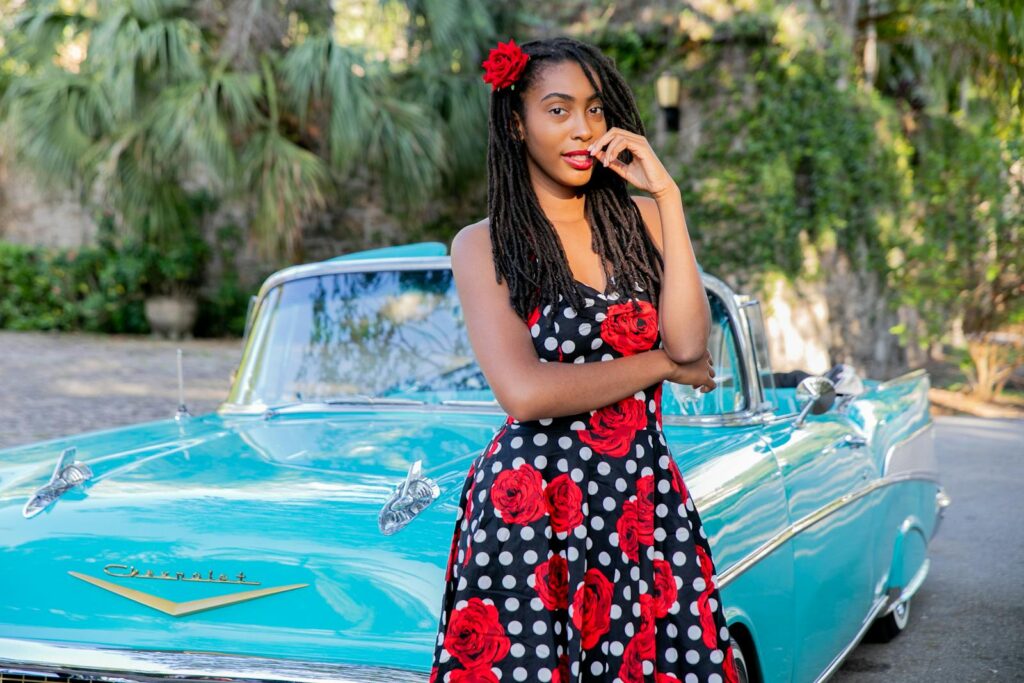Stylish woman standing beside a vintage Chevrolet in a polka dot dress with roses.