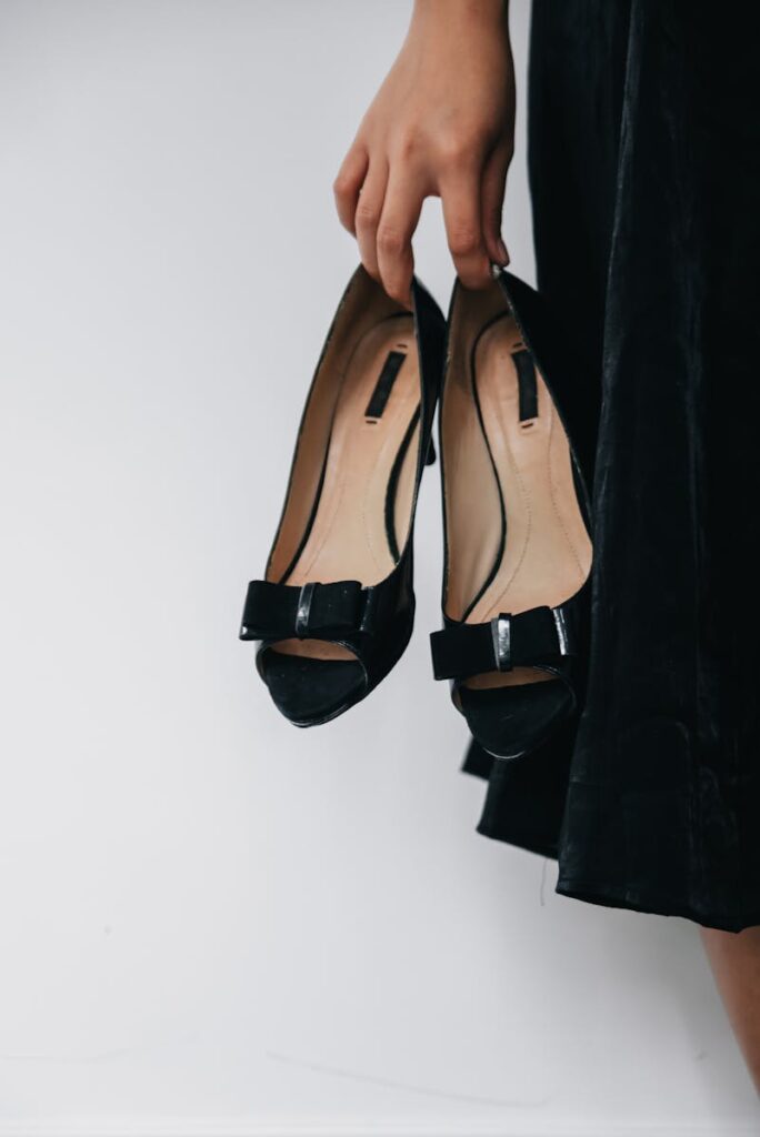 Stylish black high heels with a bow, gracefully held by a woman's hand.