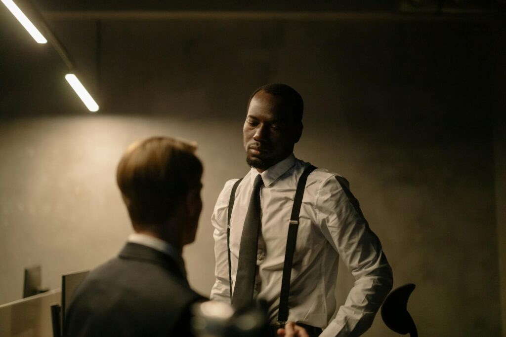 Two men in formal attire having a serious discussion in a dimly lit office with modern decor.