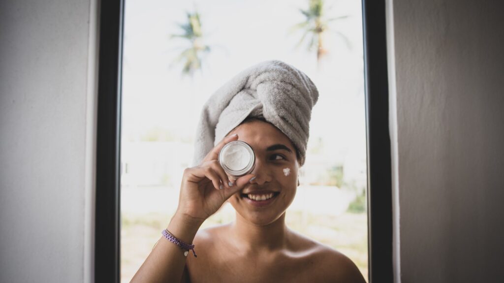Smiling woman with towel turban and face cream indoors.