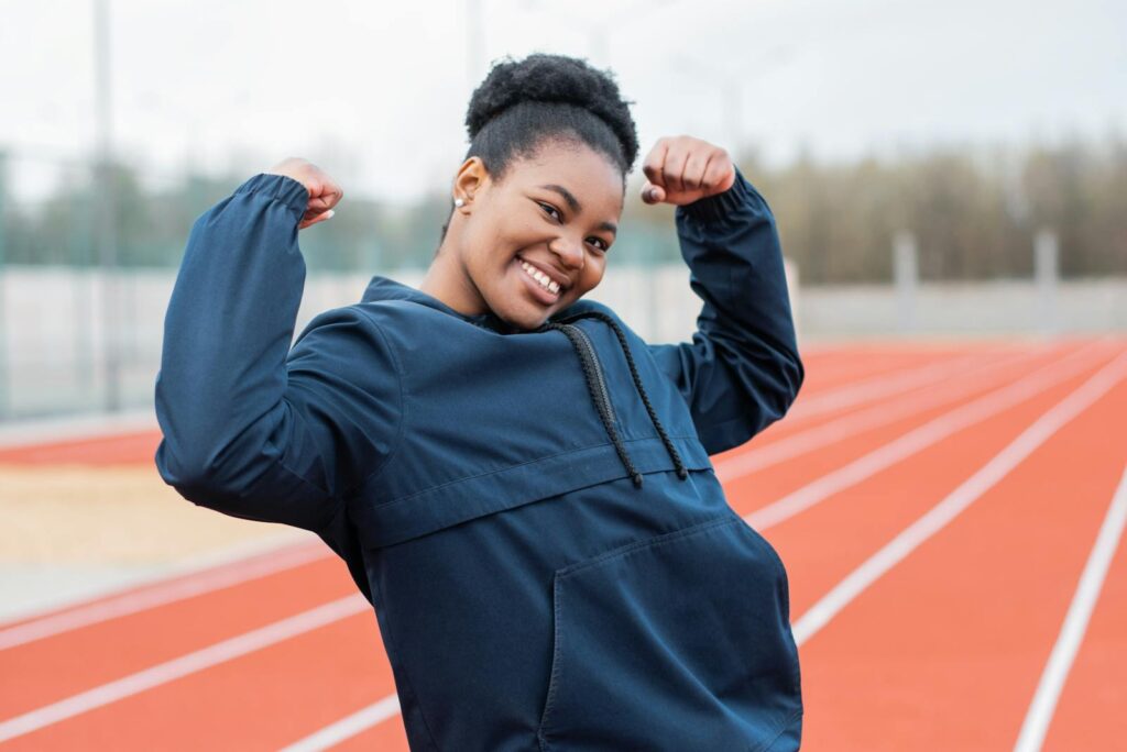 Confident woman flexing muscles on an athletic track, embodying fitness and determination.