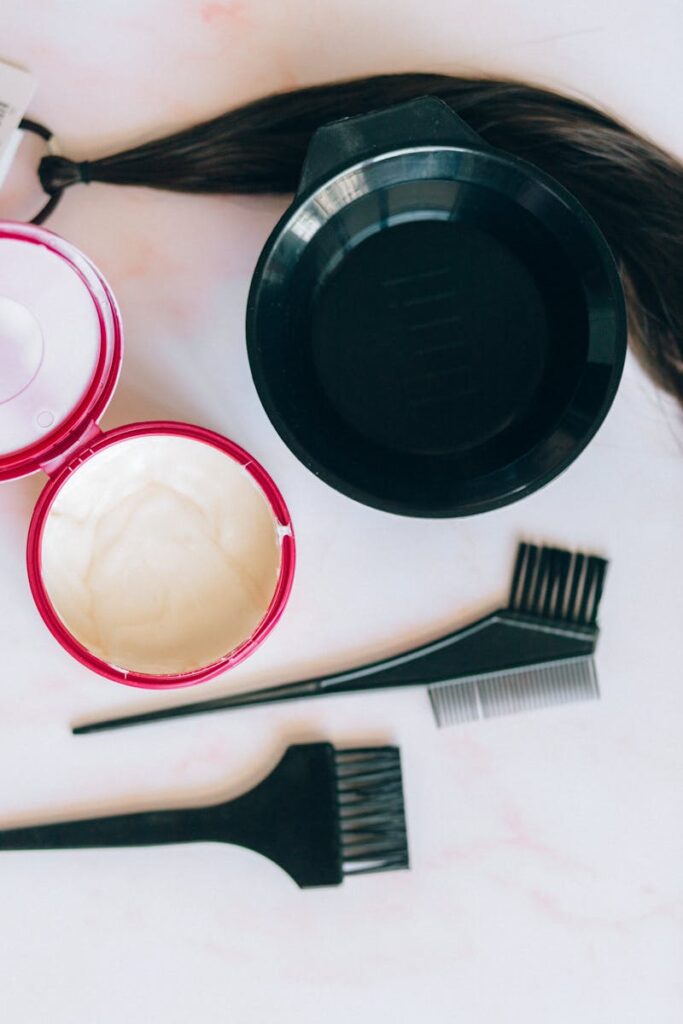 Flat lay of hair coloring essentials including bowls, brushes, and combs on a marble surface.