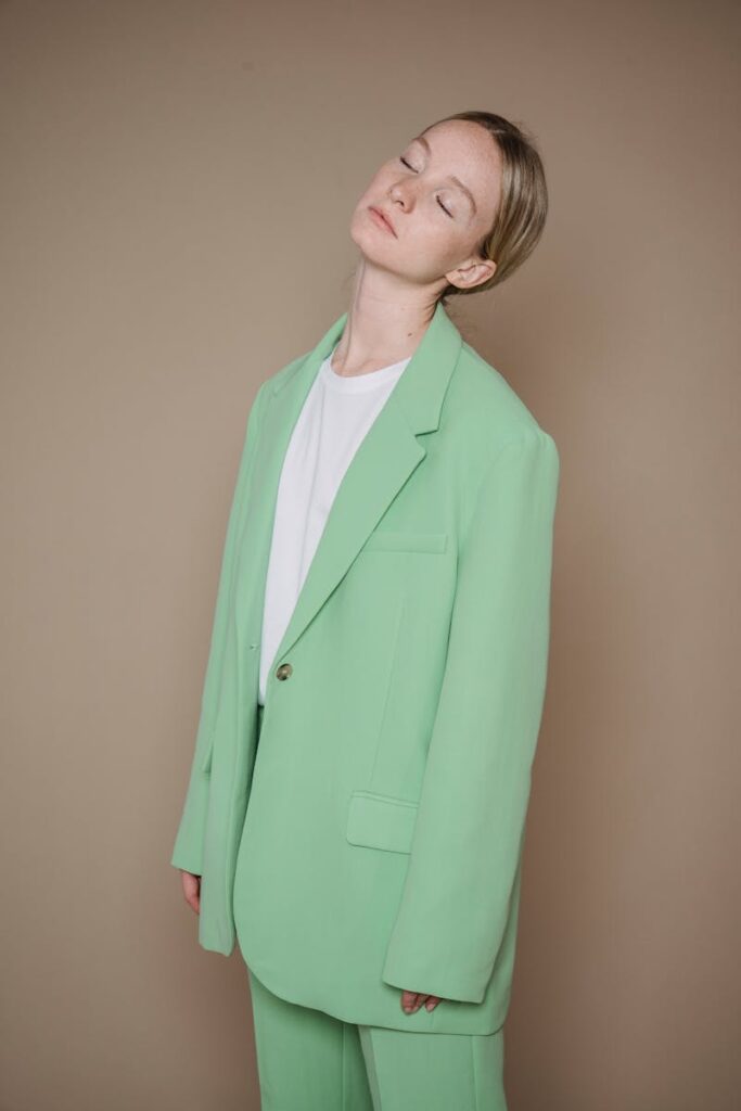 Studio shot of a woman in a green suit with closed eyes posing against a beige background.