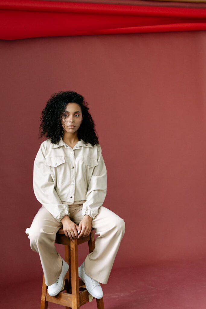 Fashionable woman sits confidently in a stylish outfit with a muted backdrop, expressing elegance and poise.