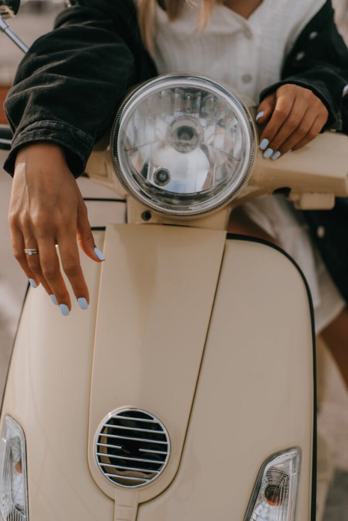 Stylish photo of a woman with painted nails leaning on a vintage beige scooter.