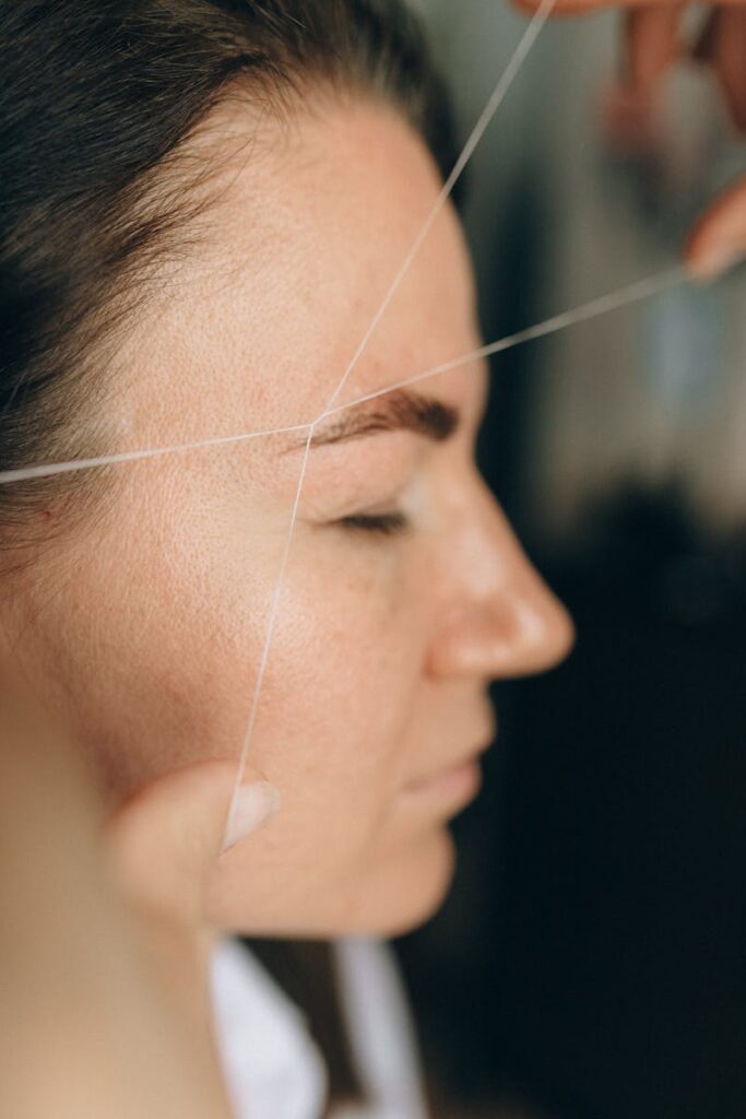 Side view of a woman receiving eyebrow threading at a salon.