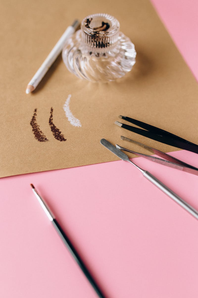 Close-up of makeup tools with swatches on a brown paper on a pink surface.