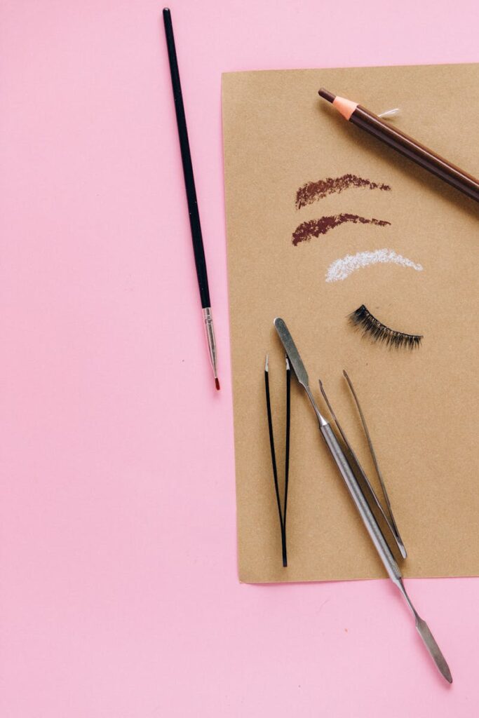 A flat lay of cosmetic tools including brushes and tweezers on a pink background.