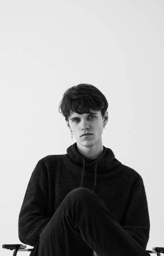 Monochrome photo of a young man in a hoodie sitting with a serious expression.