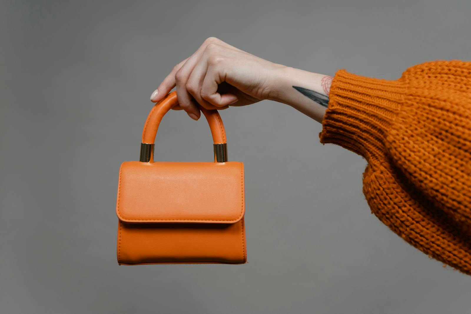A fashion-forward hand presents a vibrant orange mini shoulder bag. Perfect for modern style inspiration.