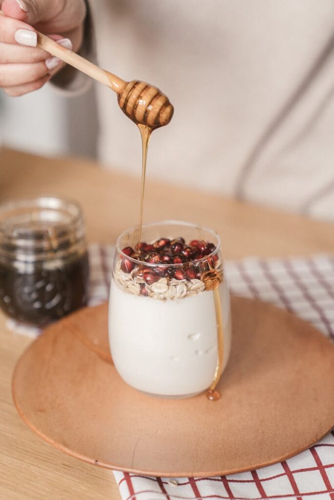 Close-up of honey drizzling onto yogurt topped with granola and pomegranate seeds.