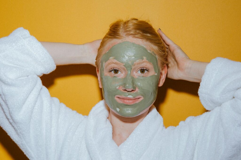 Woman enjoying self-care with a green face mask against a yellow background.