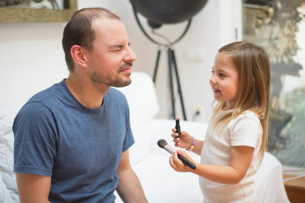 Father and daughter enjoying a joyful moment with makeup in their cozy living room.