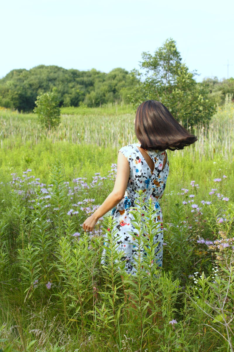 A woman in a floral dress enjoys a summer day in a lush rural field.