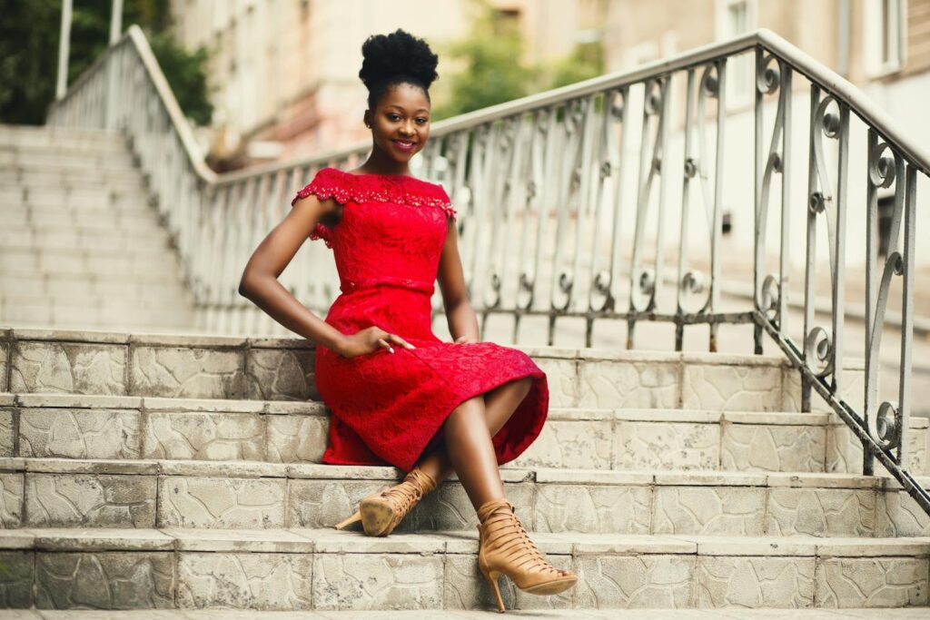 Young woman in a red lace dress sitting on outdoor steps, smiling and posing.