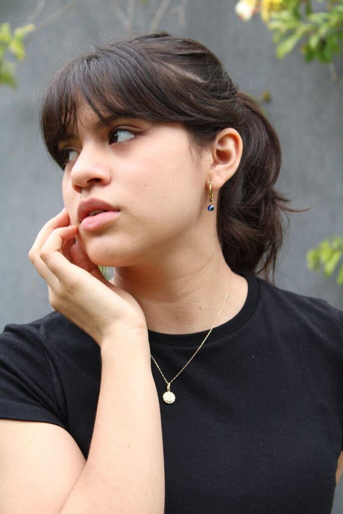 Pensive young woman in black shirt with necklace, looking away outdoors.