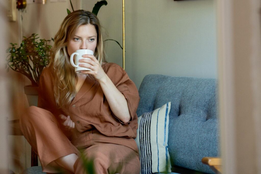 Woman in cozy loungewear sipping coffee on a couch, creating a warm, relaxing home atmosphere.