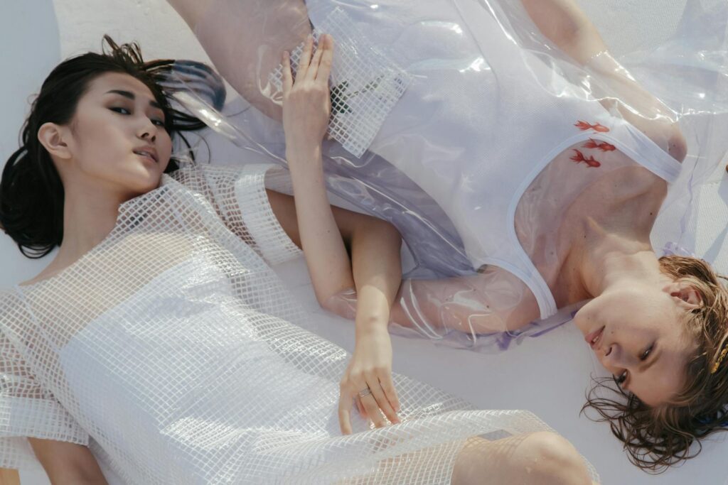 Stylish portrait featuring two young women lying in artistic, transparent fashion attire. Modern and conceptual.