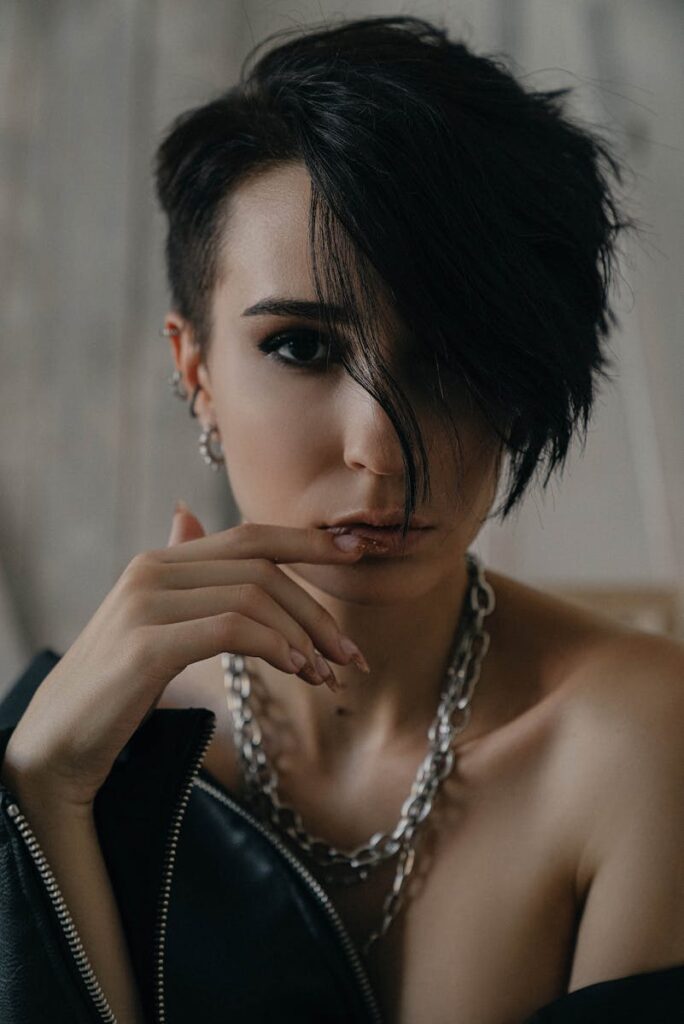 Portrait of a woman with short, dark hair and edgy style, wearing jewelry.