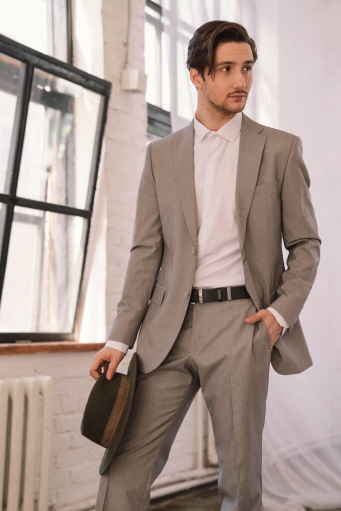 Elegant man in a gray suit holding a hat, posing indoors with a confident look.
