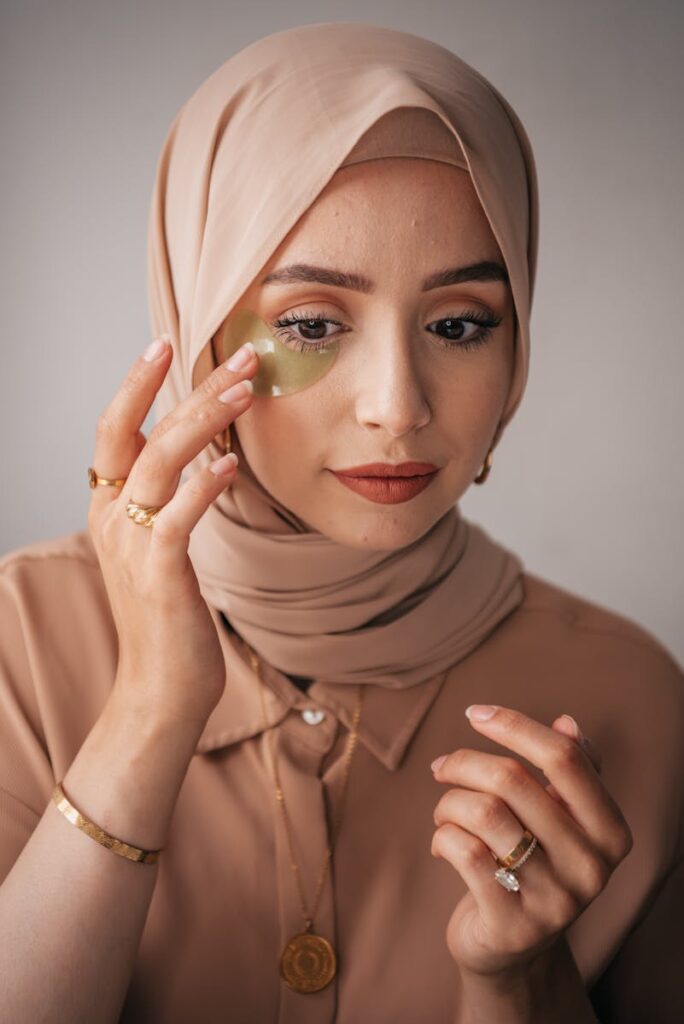 Close-up of a woman in a hijab applying an under eye patch for skincare.