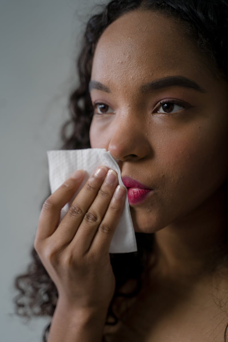 Close-up portrait of a woman gently removing lipstick with a tissue in a soft-lit indoor setting.