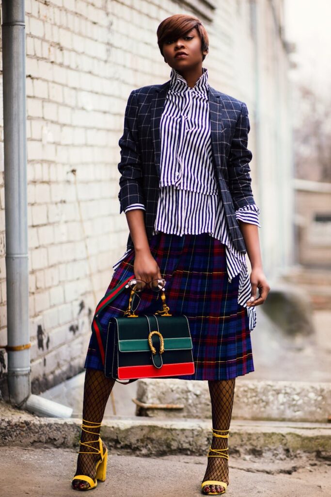 Stylish woman in striped blouse and plaid skirt posing outdoors in urban setting.
