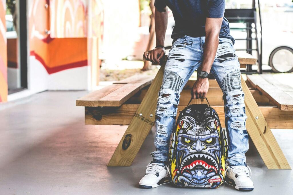 Edgy urban fashion photoshoot featuring ripped jeans and a bold graphic backpack.