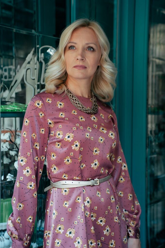 A stylish woman in a floral dress posing indoors with a thoughtful expression.