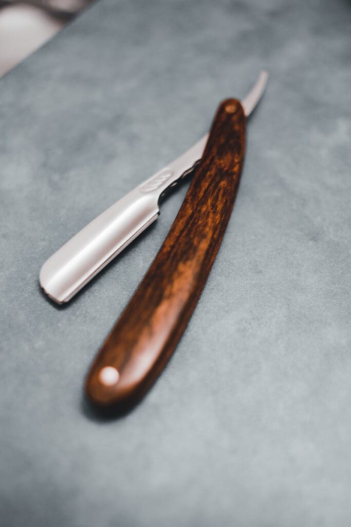 Close-up of a stylish straight razor with wooden handle on a textured surface, showing sharp blade.
