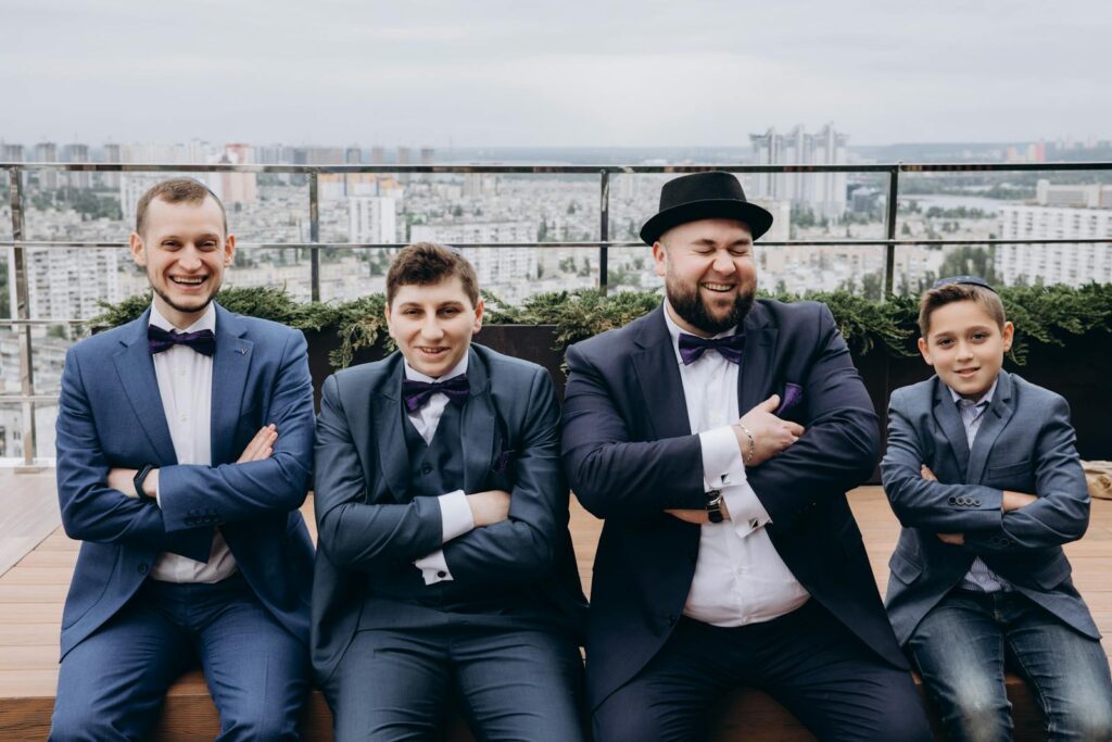 Four males in suits celebrating a special occasion with laughter on a rooftop.