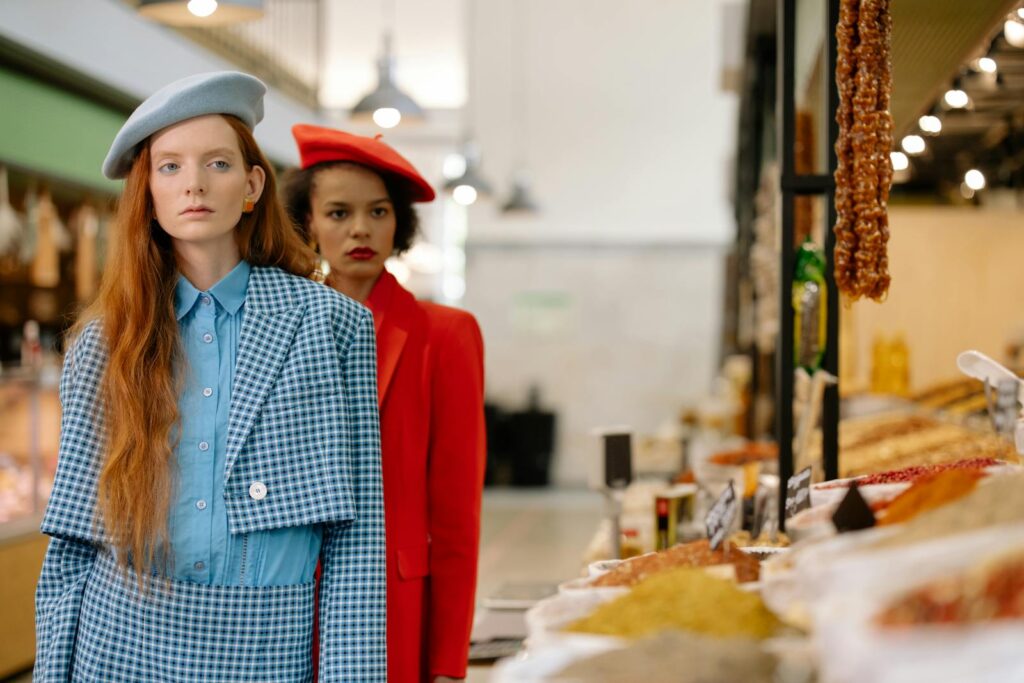 Two stylish women standing at a spice stall in an indoor market, exuding elegance