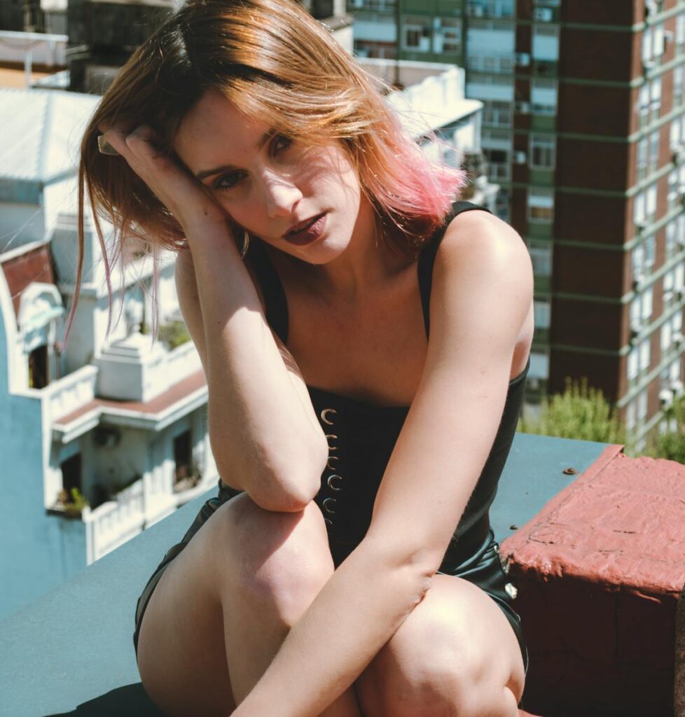 Stylish woman with pink highlights poses on a sunny rooftop, capturing urban elegance.