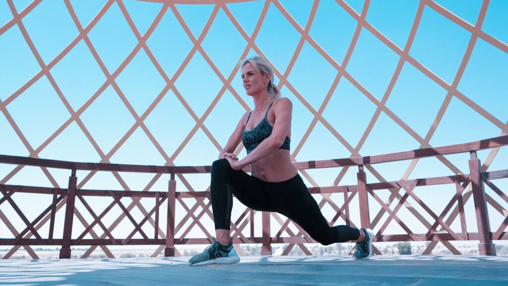 Woman performing leg lunges under a modern geometric canopy outdoors.